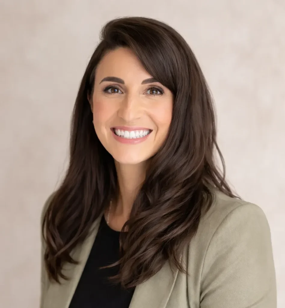 A woman in a blazer smiling in a professional headshot with a neutral background.