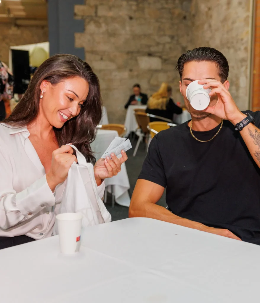 Smiling woman and man enjoying coffee and relaxing at a cafe with a rustic backdrop.