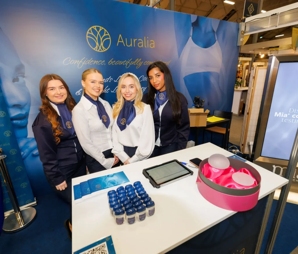 Auralia booth with smiling staff and products at a cosmetic surgery expo, showcasing confidence and innovation.