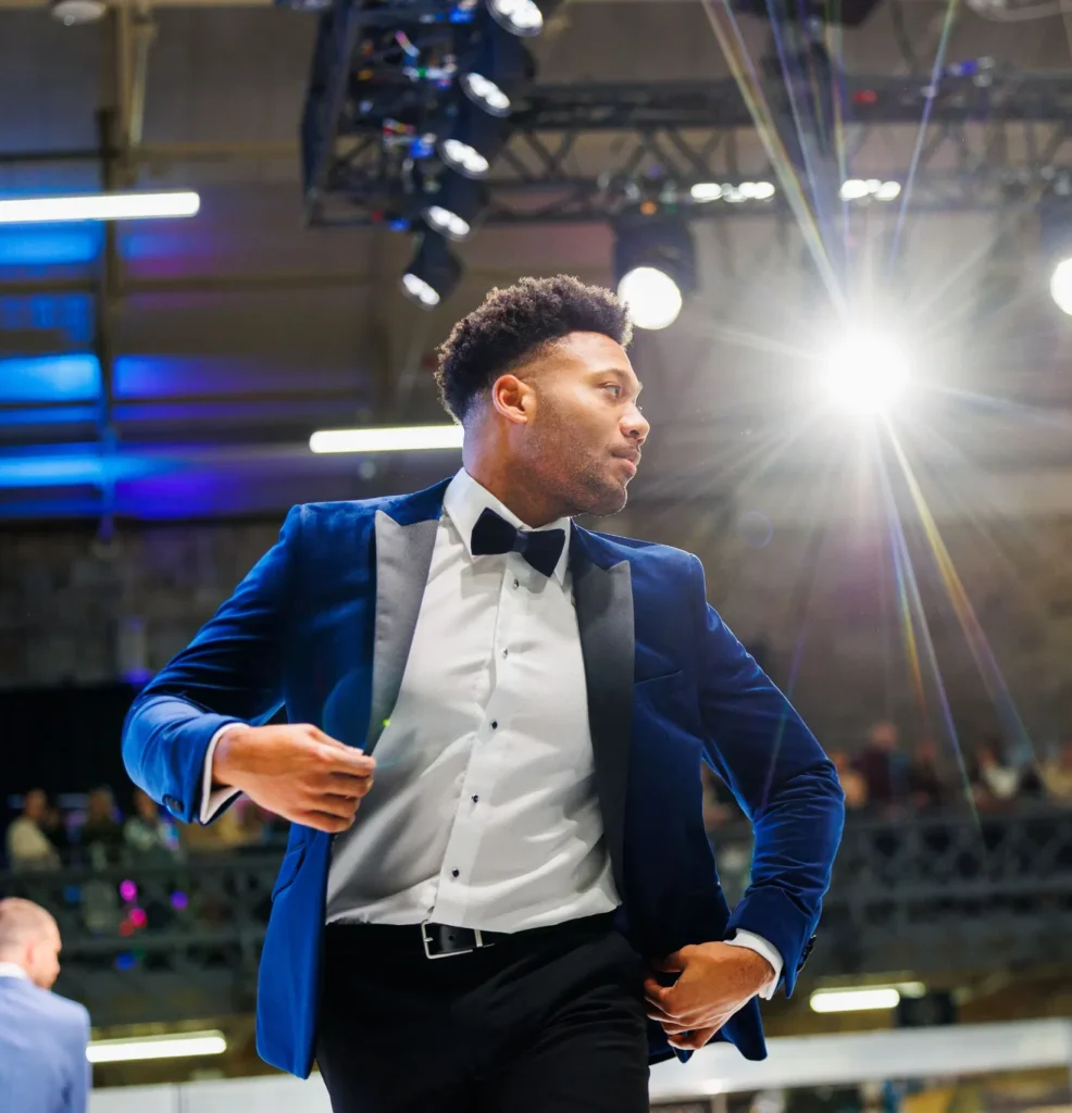 Man in a stylish blue velvet suit under bright lights, adjusting jacket at an event.