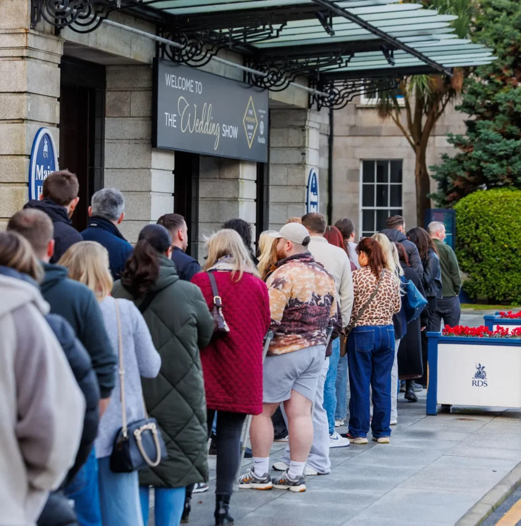 People waiting in line outside a building for a wedding show event.