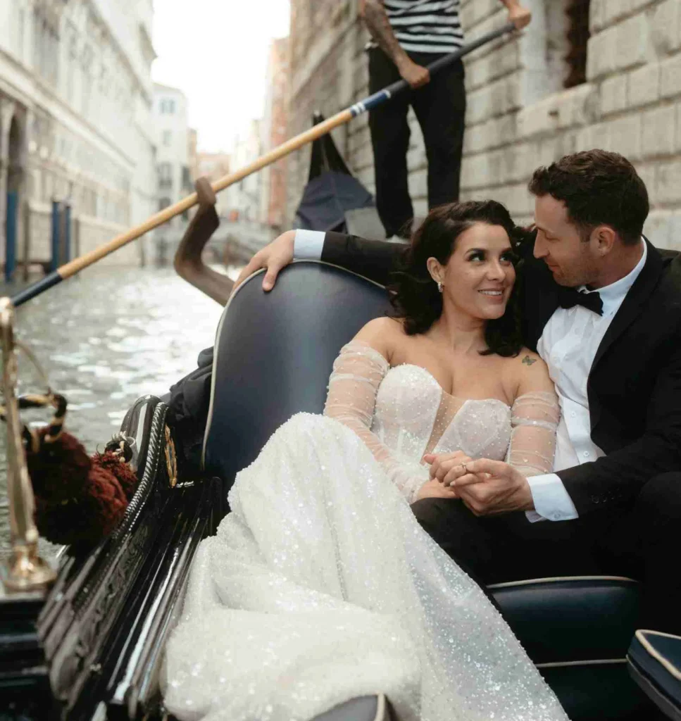 Couple in formal attire enjoying a romantic gondola ride on a serene Venice canal.