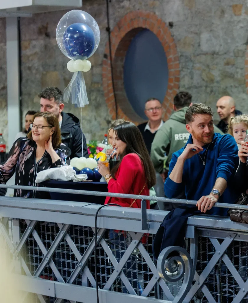 People enjoying a social gathering with drinks and balloons in a modern, industrial-style venue.