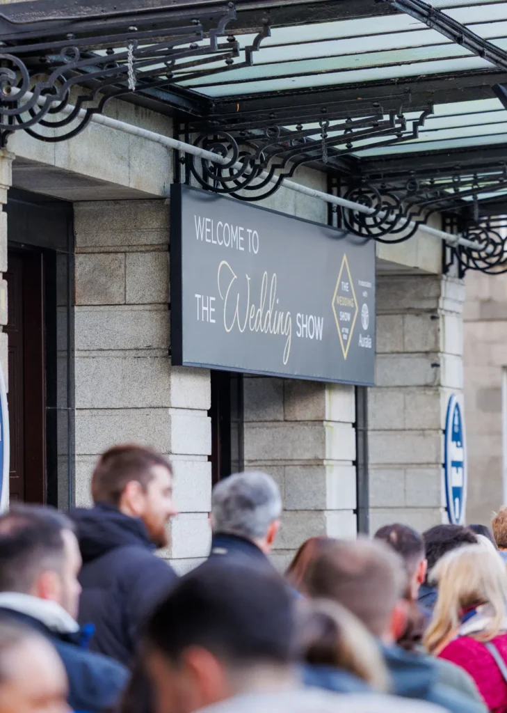 Crowd gathering at venue entrance for The Wedding Show under decorative iron canopy.