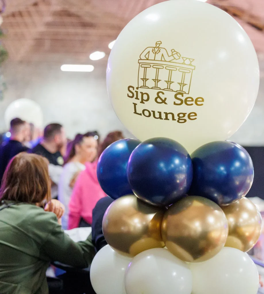 Colorful Sip & See Lounge balloons with crowd in background at event venue.