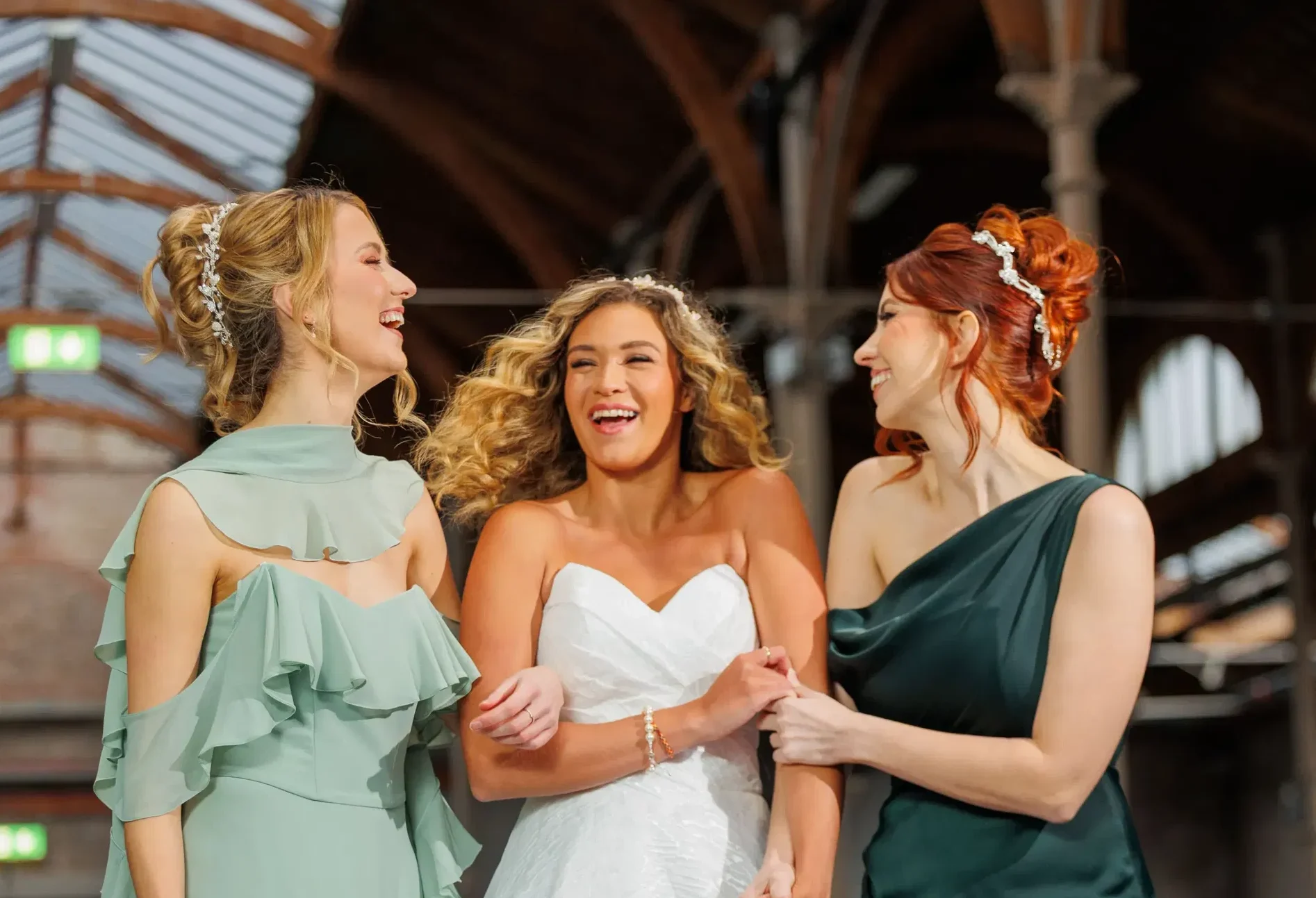 Bridesmaids and bride laugh together in stylish dresses at an indoor venue.