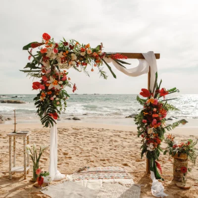 Beach wedding arch with vibrant floral decorations and ocean view.