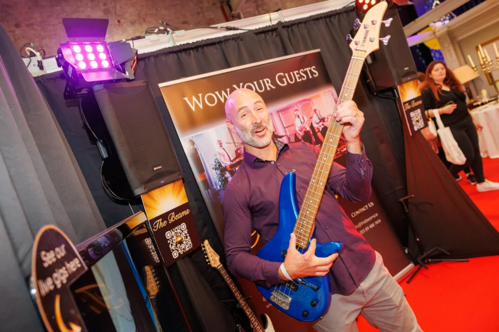 Man playing blue electric guitar at trade show booth, promoting music entertainment services.