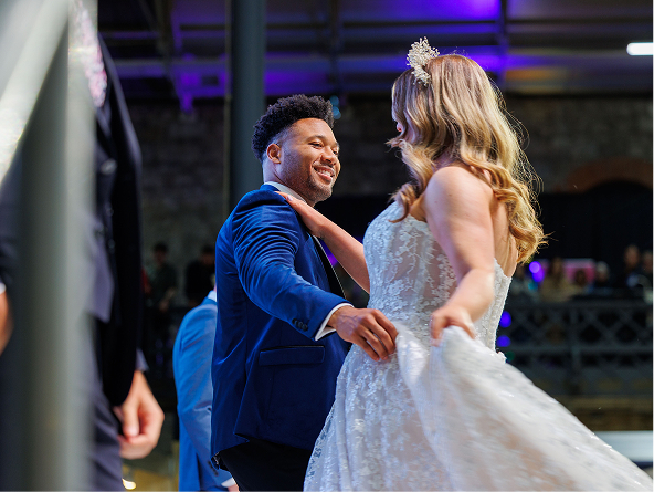 Bride and groom dancing joyfully at a wedding reception under vibrant lighting.